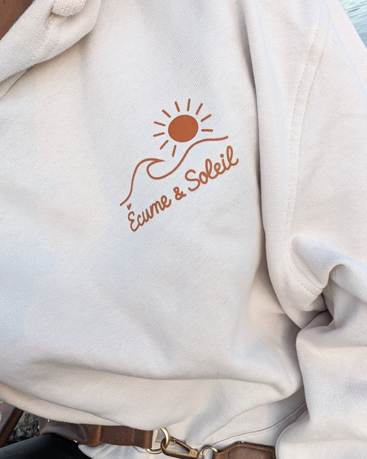 Sweat à capuche Écume & Soleil écru porté, logo soleil et vague et signature au cœur