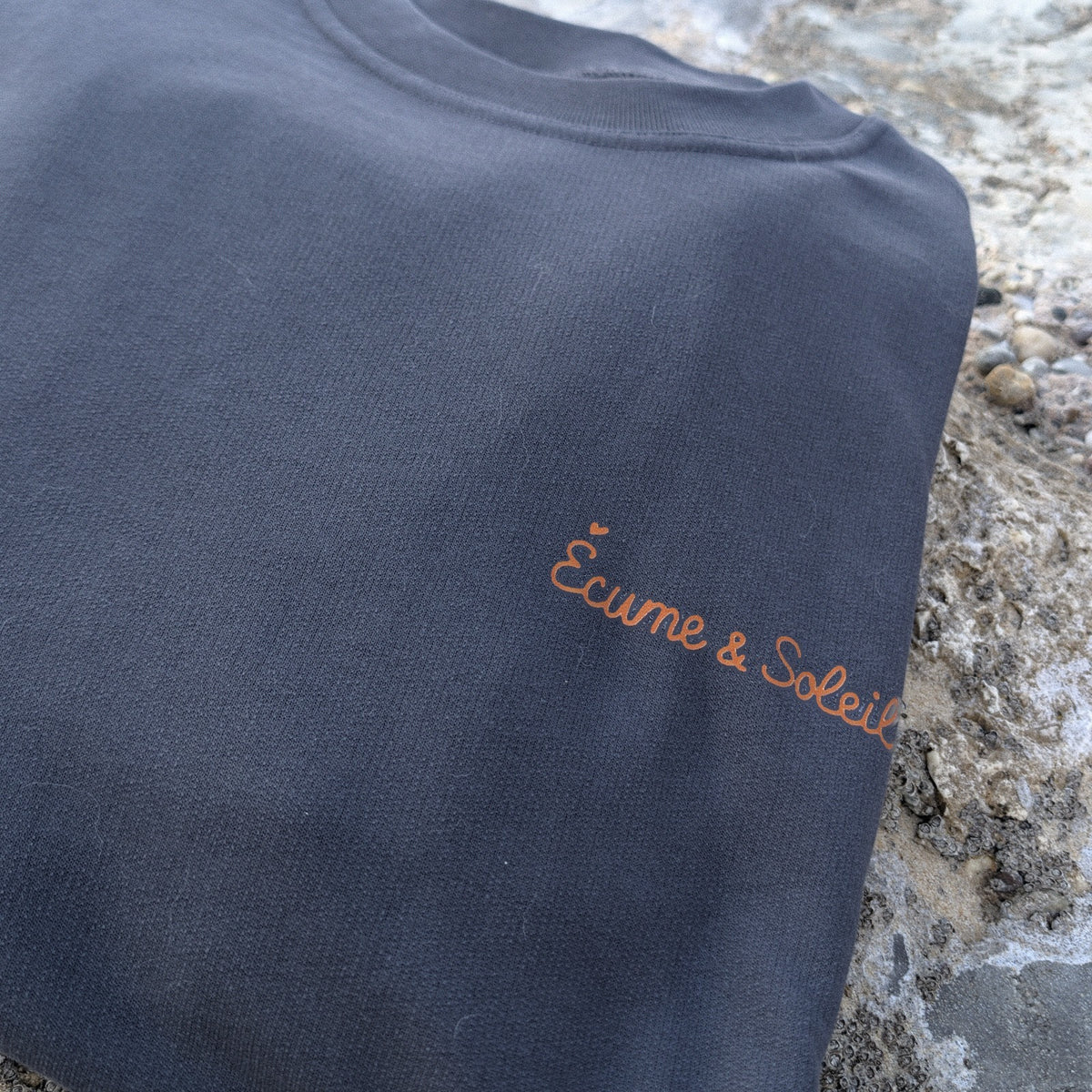 Pull Le Basique anthracite, détail du nom Écume & Soleil marqué au cœur, l'accent du É en petit cœur