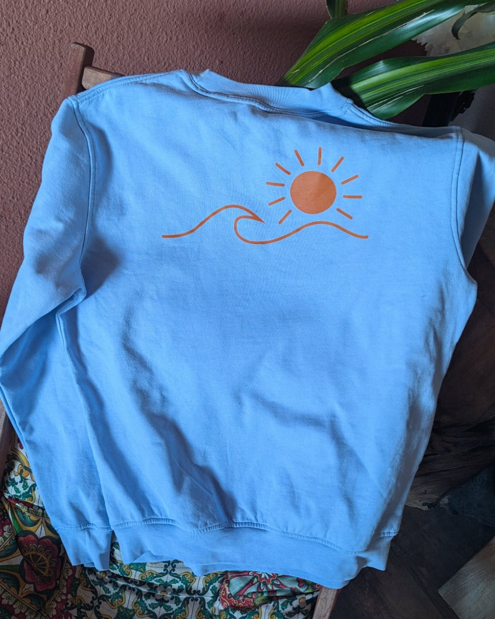 Pull Le Basique bleu ciel vu de dos, logo soleil & vague marqué en grand