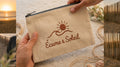 Pochette Libre Ensemble Écume & Soleil en coton sable tenue en main, logo soleil et vague