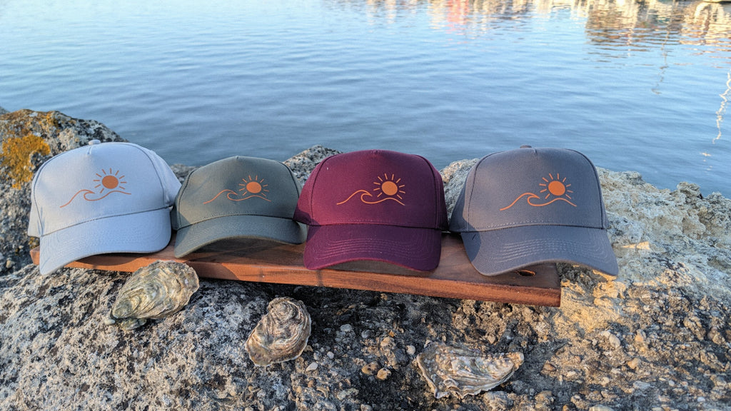 Les quatre casquettes Écume & Soleil alignées au port de Gujan : gris clair, kaki, bordeaux et gris foncé