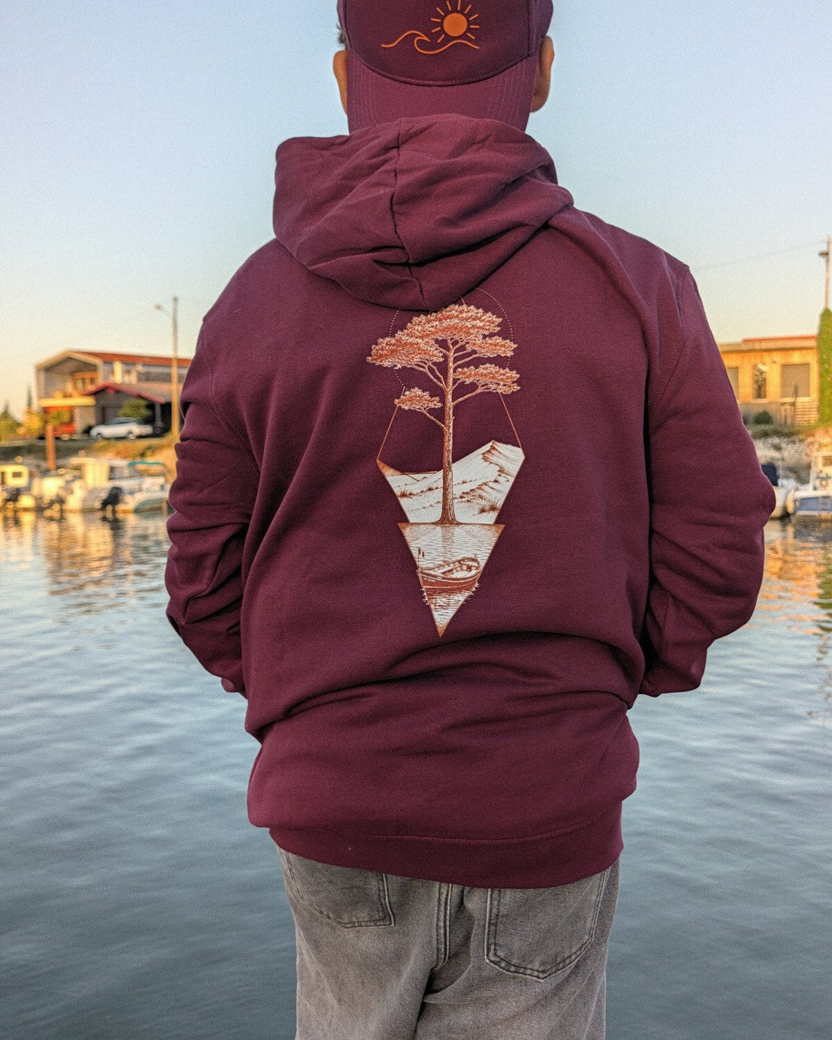 Sweat à capuche Île & Pins bordeaux vu de dos, motif pin et pinasse marqué en grand, au port de Gujan