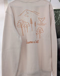 Sweat Écume & Soleil Esprit Bassin écru, vu de dos sur le portant : forêt de pins, dune et queue de baleine, signature sous le motif