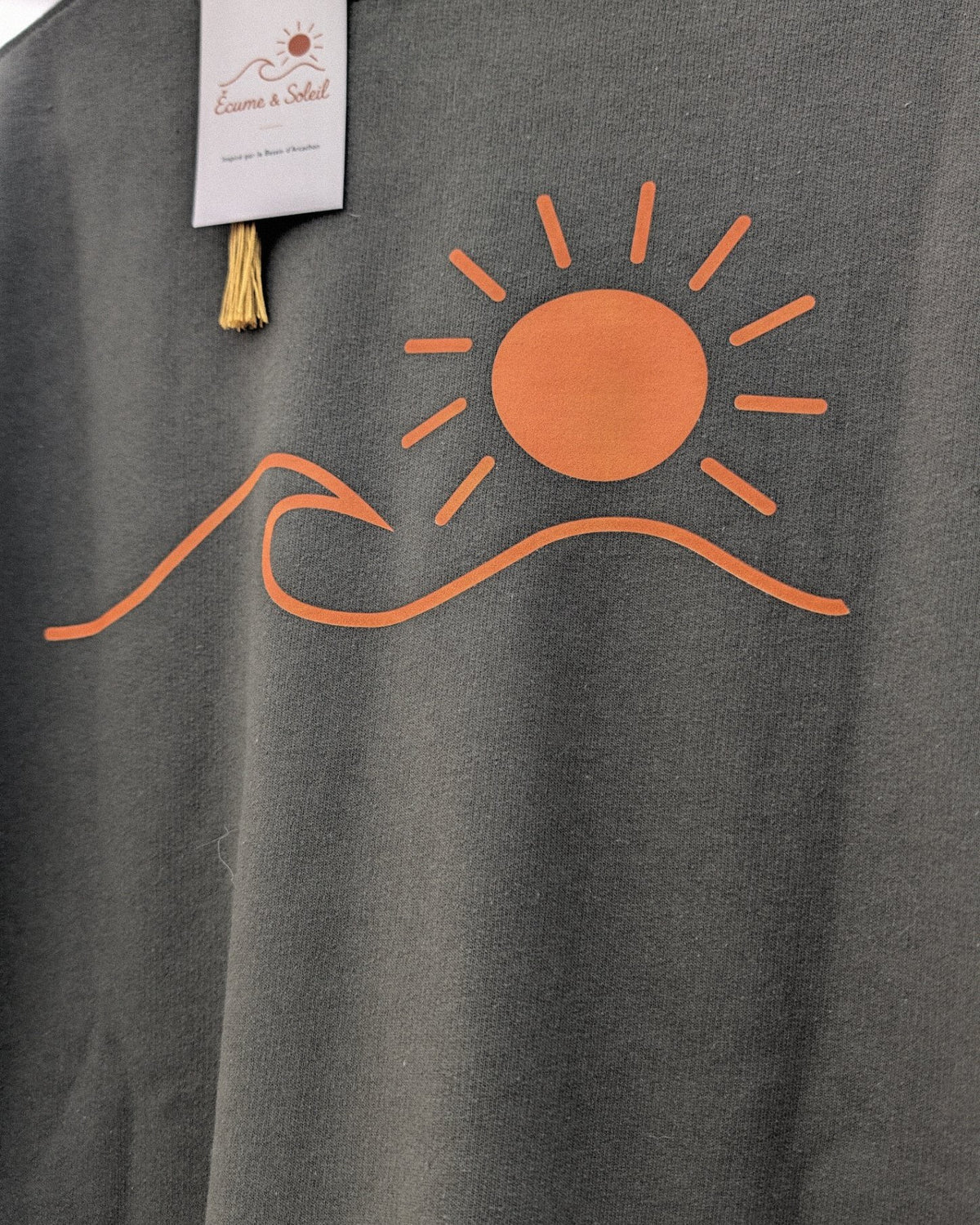 Sweat Écume & Soleil Le Basique kaki, vu de dos sur le portant : le soleil et la vague marqués en grand