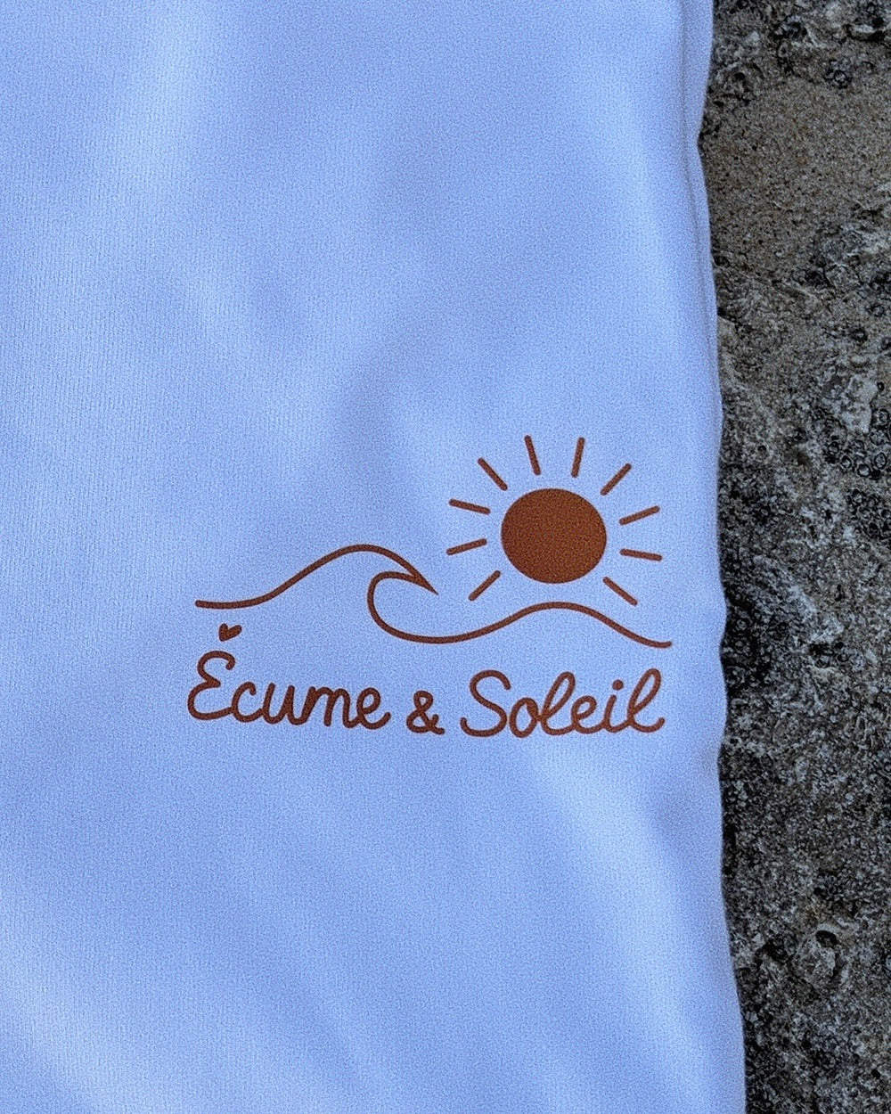 T-shirt Écume & Soleil blanc, gros plan : logo soleil & vague et signature Écume & Soleil marqués au cœur, l'accent du É en petit cœur