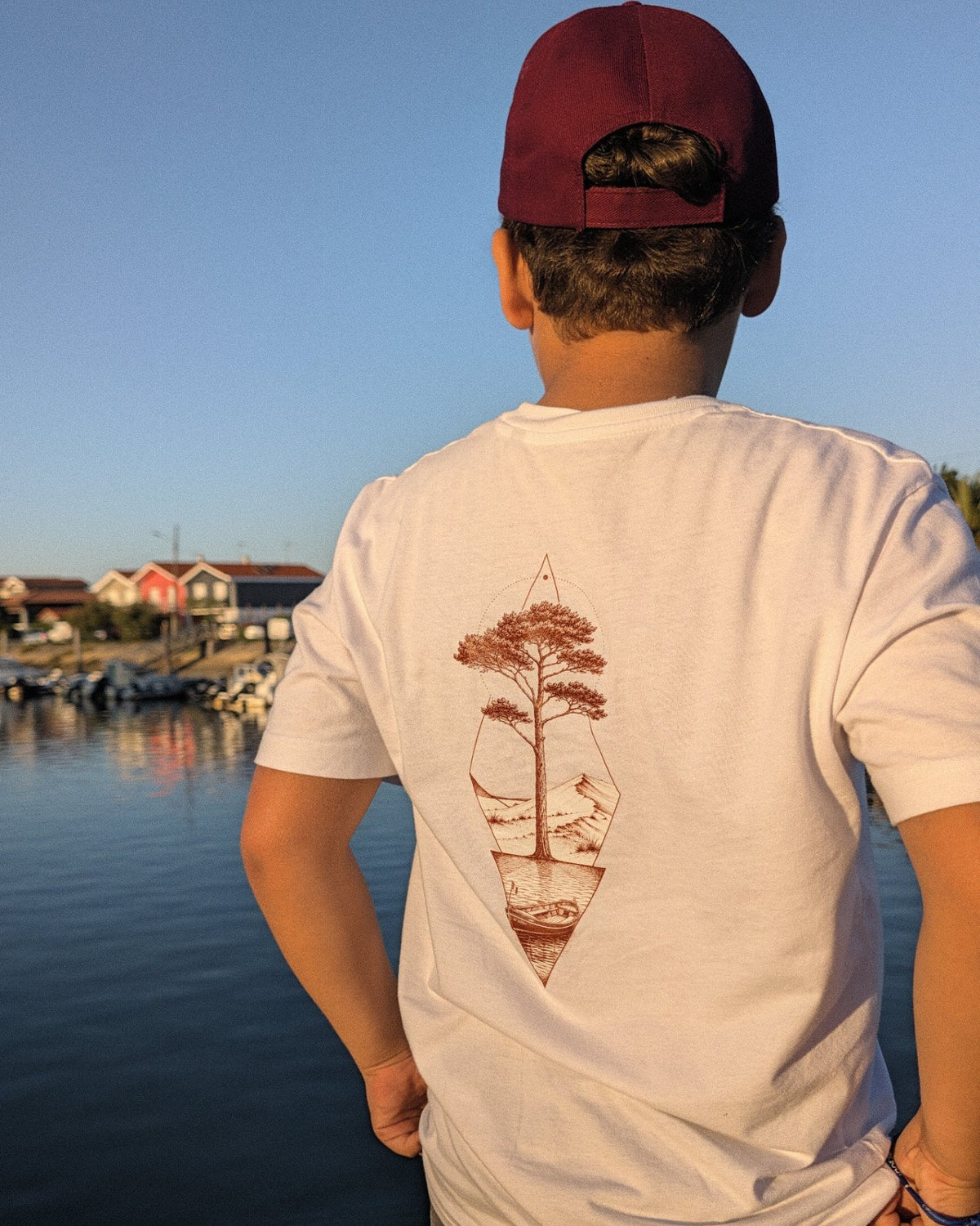 T-shirt Île & Pins blanc porté de dos au coucher du soleil, motif sépia au centre du dos
